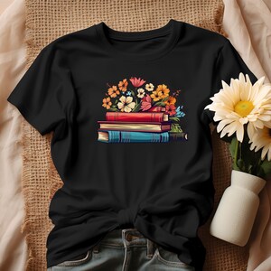 K&ouml;nnte beinhalten: Schwarzes T-Shirt mit einem Aufdruck einer Stapel B&uuml;cher mit bunten Blumen darauf.
