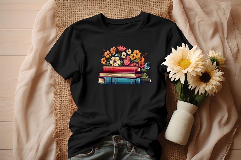 K&ouml;nnte beinhalten: Schwarzes T-Shirt mit einem Aufdruck einer Stapel B&uuml;cher mit bunten Blumen darauf.