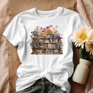 K&ouml;nnte beinhalten: Wei&szlig;es T-Shirt mit einem Motiv einer mit B&uuml;chern gef&uuml;llten B&uuml;cherregals, das mit Blumen verziert ist. Die Blumen sind in verschiedenen Farben, darunter Lila, Rosa, Orange und Gelb.