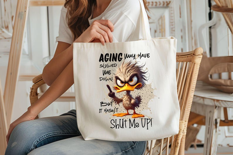 May include: White canvas tote bag with a cartoon duck illustration and the text "Aging may have slowed me down but it hasn't shut me up!"