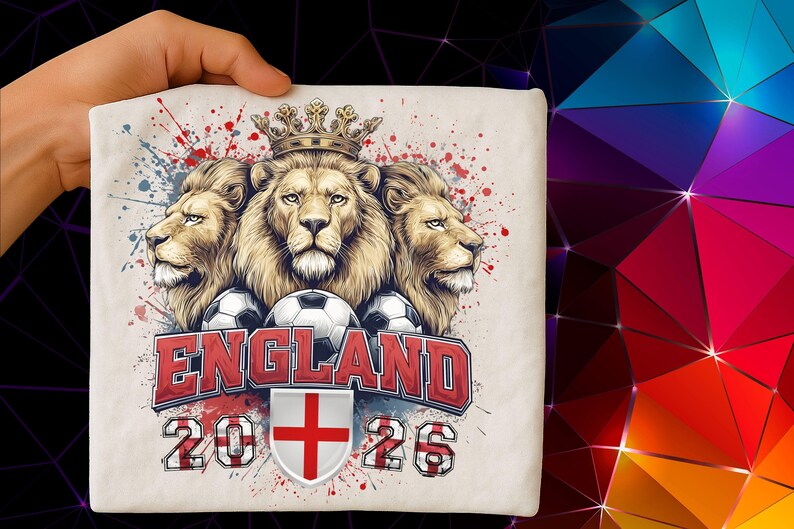 Puede incluir: Una camiseta color crema con un dise&ntilde;o que presenta tres leones coronados, balones de f&uacute;tbol y la palabra "ENGLAND" en rojo. El dise&ntilde;o incluye los a&ntilde;os "2026" y un escudo con una cruz roja.