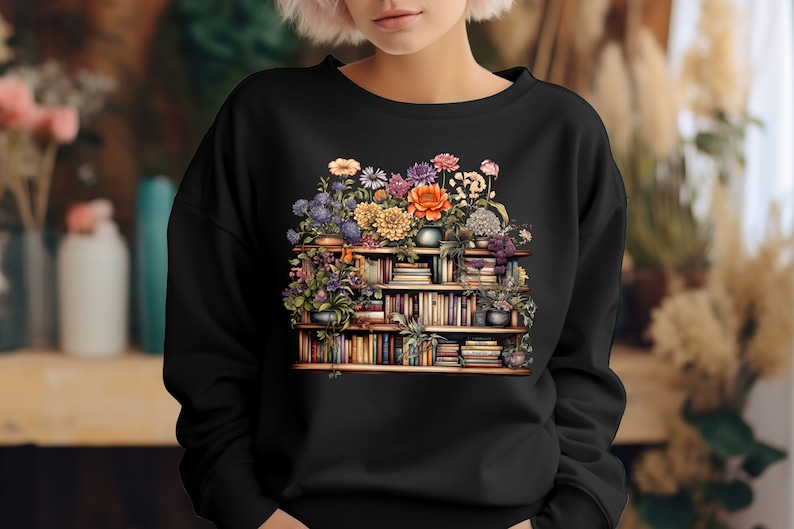 K&ouml;nnte beinhalten: Ein schwarzes Sweatshirt mit einem Aufdruck einer mit B&uuml;chern und Blumen gef&uuml;llten B&uuml;cherregals. Die Blumen sind in verschiedenen Farben, darunter Orange, Gelb, Rosa und Lila.