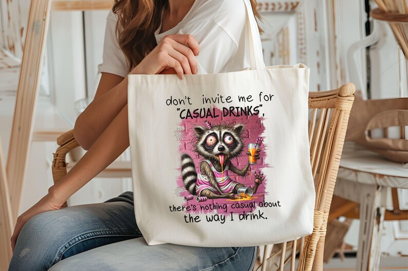 May include: White canvas tote bag with a cartoon raccoon drinking from a glass. The text on the bag reads "don't invite me for 'CASUAL DRINKS', there's nothing casual about the way I drink."
