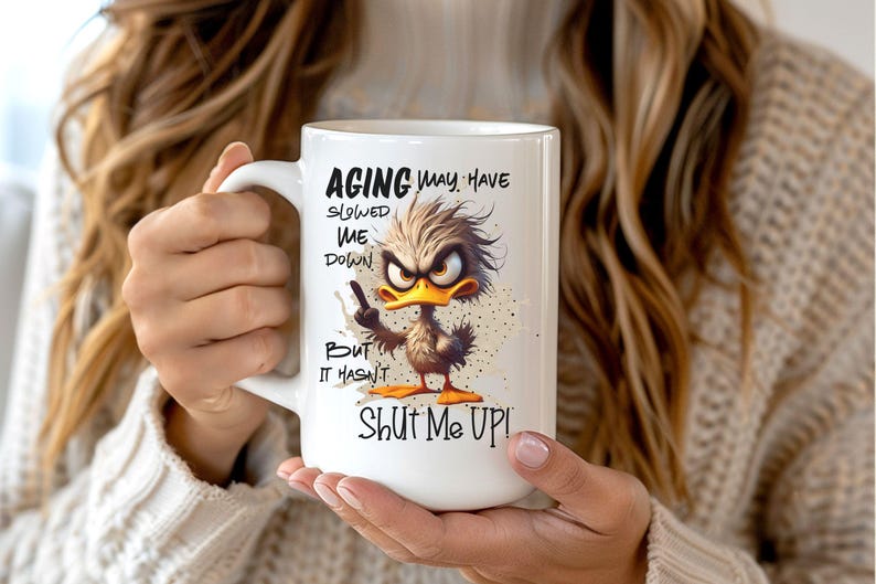 May include: White ceramic mug with a funny cartoon duck and the text "Aging may have slowed me down but it hasn't shut me up!"