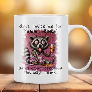 May include: White ceramic mug with a cartoon raccoon drinking from a can and a glass. The mug has the text "don't invite me for "CASUAL DRINKS", there's nothing casual about the way I drink."