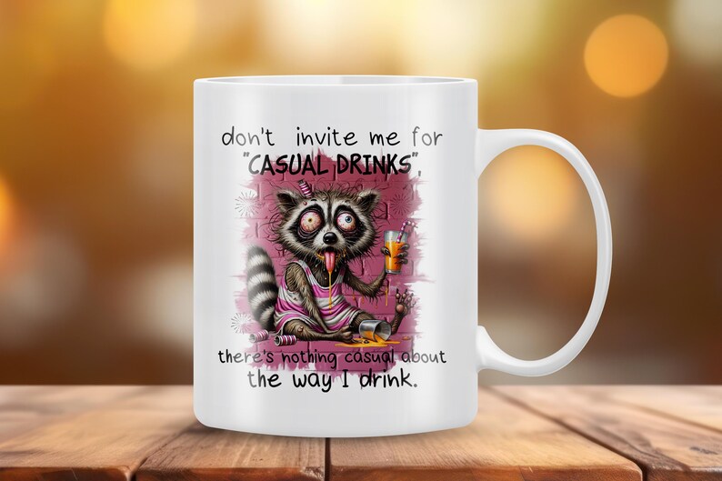 May include: White ceramic mug with a cartoon raccoon drinking from a can and a glass. The mug has the text "don't invite me for "CASUAL DRINKS", there's nothing casual about the way I drink."