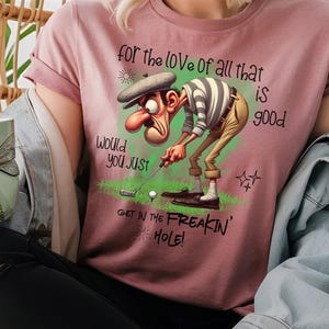 May include: A pink t-shirt with a cartoon golfer and the text "for the love of all that is good would you just get in the freakin' hole!"