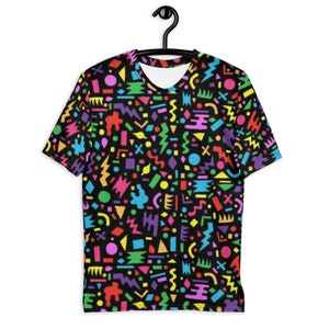 May include: A black t-shirt with a colorful geometric pattern. The pattern includes circles, squares, triangles, and lightning bolts in various colors, including red, yellow, green, blue, and purple.