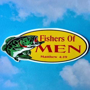 May include: An oval sticker with a yellow background featuring a green and white fish on the left side. The text reads Fishers Of MEN in red letters, with Matthew 4:19 printed in smaller red text below. The sticker has a white border.