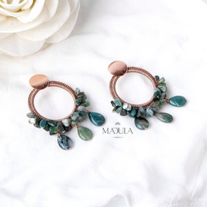 Può includere: Un paio di orecchini a cerchio in oro rosa con pietre di agata verde. Gli orecchini sono realizzati con un design avvolto in filo e hanno una goccia di agata verde pendente. Gli orecchini sono etichettati "Madula Jewels".