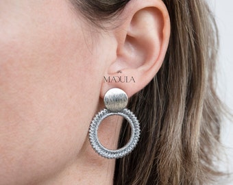May include: Silver hoop earrings with a textured round charm. The earrings are made of a woven metal design.