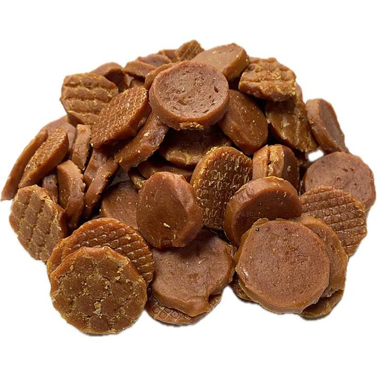 May include: A pile of brown, circular dog treats with various textures. Some treats are round, others are rectangular, and some have a waffle-like pattern. The treats are a medium brown color and appear to be crunchy.