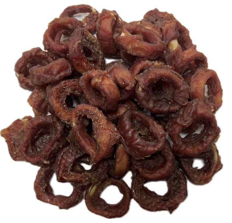 May include: A pile of dried, reddish-brown, ring-shaped treats, possibly pet food or snacks, against a white background. The treats have a slightly wrinkled texture and a dark, rich color, suggesting they are savory and possibly chewy.