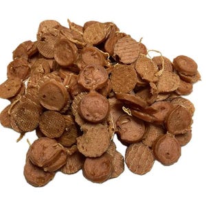 May include: A pile of brown, circular dog treats with various textures. Some treats are round, others are flat, and some have grill marks. The treats are scattered on a white background.