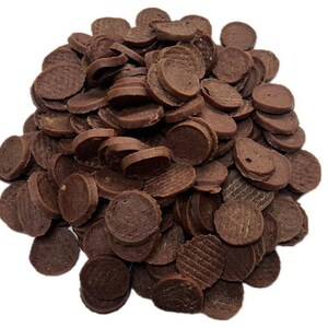 May include: A pile of small, round, dark brown dog treats. The treats are disc-shaped, with some showing textured patterns on their surfaces. The image is taken against a white background, highlighting the treats.