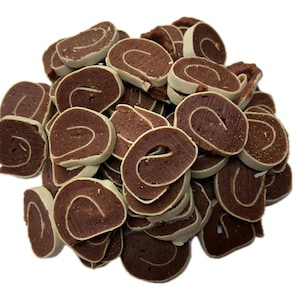May include: A pile of dog treats, each a dark brown color with a white outer edge and a light-colored swirl in the center. The treats are arranged in a random pattern against a white background.