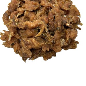 May include: A pile of dried, light brown fish snacks. The treats have a textured appearance and are arranged in a heap against a white background. The fish pieces appear to be small and crunchy.