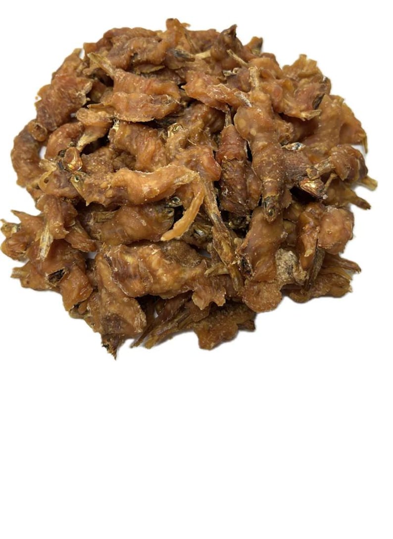 May include: A pile of dried, light brown fish snacks. The treats have a textured appearance and are arranged in a heap against a white background. The fish pieces appear to be small and crunchy.