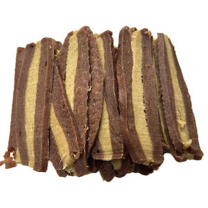 May include: A stack of dog treats with alternating layers of brown and tan colors. The treats are cut into rectangular shapes and have a textured appearance. The treats are likely made of meat or a similar ingredient.