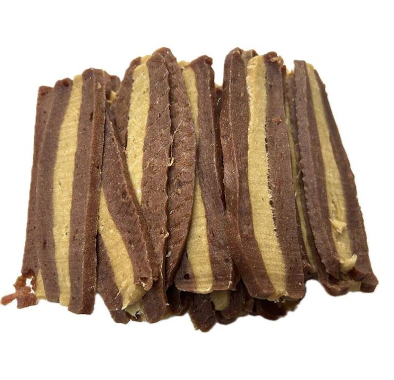May include: A stack of dog treats with alternating layers of brown and tan colors. The treats are cut into rectangular shapes and have a textured appearance. The treats are likely made of meat or a similar ingredient.