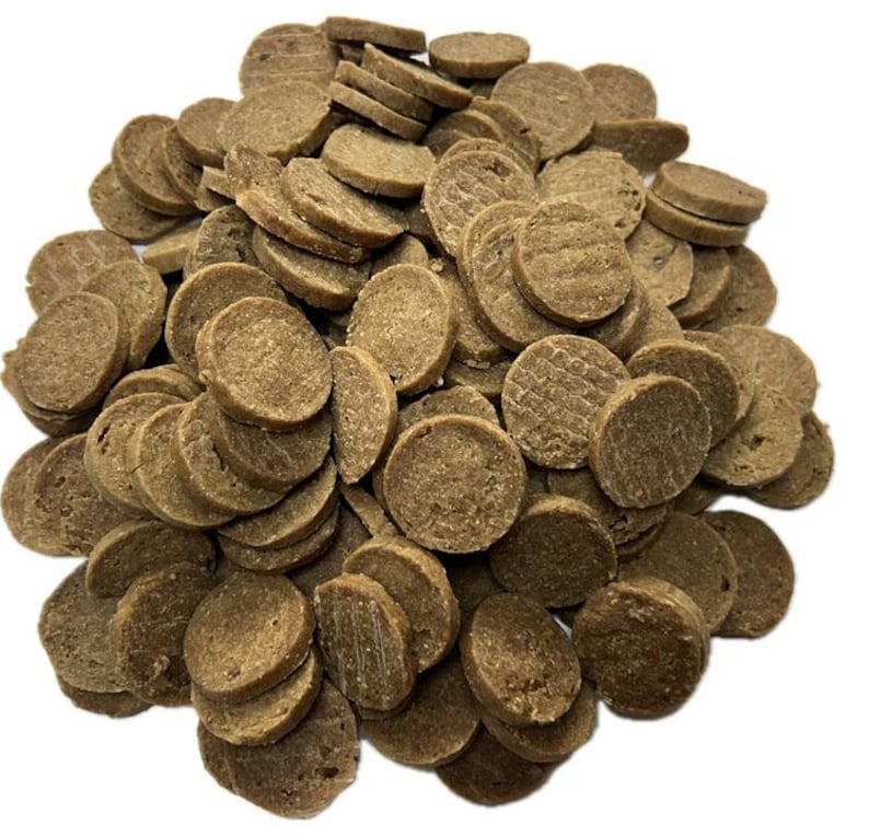 May include: A pile of small, round, brown pet treats. The treats have a slightly textured surface and are stacked in a random arrangement. The treats appear to be dry and are likely a type of dog or cat food.