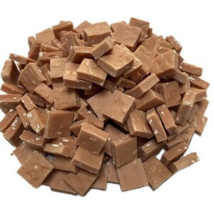 May include: A pile of small, square-shaped pieces of fudge. The fudge is a light brown color with visible white specks throughout. The pieces are scattered, creating a textured and appetizing appearance.