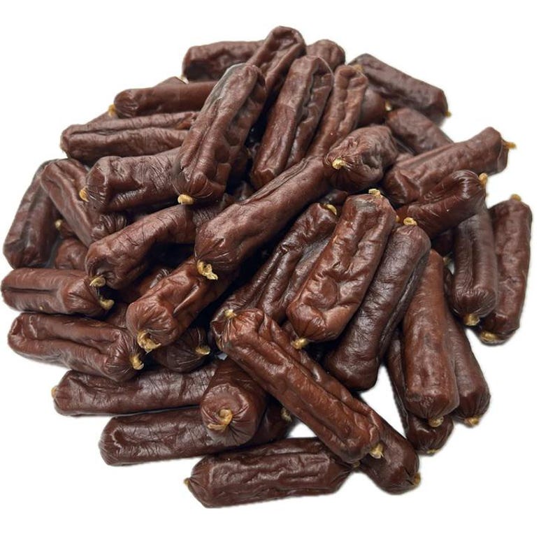 May include: A pile of dark brown sausages with a slightly wrinkled texture. Each sausage is individually wrapped at both ends. The sausages are tightly packed together, creating a dense arrangement against a white background.