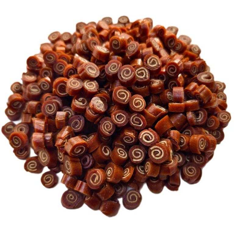 May include: A pile of brown, spiral-shaped dog treats. Each treat has a dark brown exterior and a lighter, tan-colored interior, resembling a cinnamon roll. The treats are scattered against a white background.