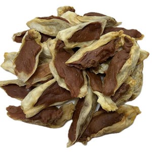 May include: A pile of dog treats, featuring a light tan outer layer and a dark brown filling. The treats have a unique shape, resembling small, open pockets. The background is plain white, highlighting the treats.