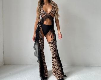May include: A woman wearing a leopard print bikini top with a black mesh overlay and matching leopard print chaps with black mesh trim.