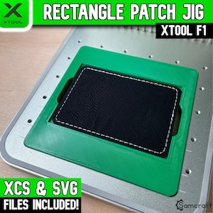 Puede incluir: Una plantilla rectangular verde para parches, diseñada para la máquina láser xTool F1. La plantilla se sitúa sobre una base de metal plateado y sostiene un parche rectangular negro con bordes cosidos en blanco. El texto indica RECTANGLE PATCH JIG, XTOOL F1, XCS & SVG FILES INCLUDED.