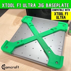 May include: A green X-shaped jig baseplate attachment for the xTool F1 Ultra laser machine. The accessory features a bright green plastic frame with four corner brackets secured by metal screws, mounted onto a silver metal grid baseplate.