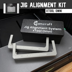 May include: A Samcraft Jig Alignment System kit for the xTool Omni, featuring a black rectangular storage box with white text and two grey U-shaped alignment tools. Each tool is clearly labeled with the Samcraft logo and OMNI JIG ALIGNMENT SYSTEM.