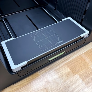 May include: A black rectangular alignment jig system with light grey corner brackets and a central circular grid pattern printed on the surface. The text "OMNI JIG ALIGNMENT SYSTEM" is visible on the left side, and "FATMAT" is on the right.