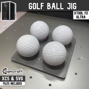 May include: A gray golf ball jig holding four white golf balls. The jig has a rectangular shape with circular indentations for each ball. The text "GOLF BALL JIG" and "XTOOL F2 ULTRA" are visible. The text "XCS & SVG FILES INCLUDED" is also visible.