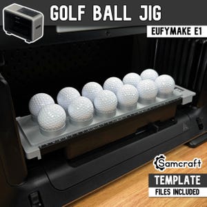 Könnte beinhalten: Eine graue Golfball-Vorrichtung aus Kunststoff für den EufyMake E1 mit zwölf kreisförmigen Vertiefungen, die weiße Golfbälle mit Grübchen halten. Die Vorrichtung enthält ein aufgedrucktes Lineal an der Vorderkante und ist mit dem Text GOLF BALL JIG, EUFYMAKE E1 und Samcraft TEMPLATE FILES INCLUDED beschriftet.