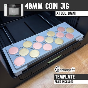 May include: A grey 40mm coin jig for the xTool Omni alignment system, featuring multiple circular cutouts holding alternating gold and rose gold metallic coins. The Samcraft template includes text labels and is positioned inside a laser machine.