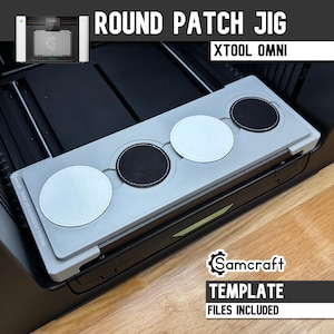 Puede incluir: Una plantilla de alineación rectangular de color gris claro para parches redondos, con cuatro recortes circulares que contienen dos parches blancos y dos negros. La plantilla está etiquetada como Samcraft Omni Jig Alignment System para xTool Omni.
