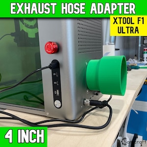 May include: A bright green 4 inch exhaust hose adapter attached to the side of a silver XTOOL F1 ULTRA laser machine. The machine features a red emergency stop button, a black control panel with USB ports, and a black power cable connected to the base.
