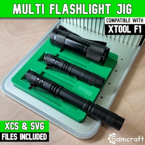 Puede incluir: Una plantilla verde para linternas con tres linternas negras de diferentes tamaños colocadas en ranuras moldeadas. El texto dice MULTI FLASHLIGHT JIG, COMPATIBLE WITH XTOOL F1 y XCS & SVG FILES INCLUDED. La plantilla está sobre una base metálica.