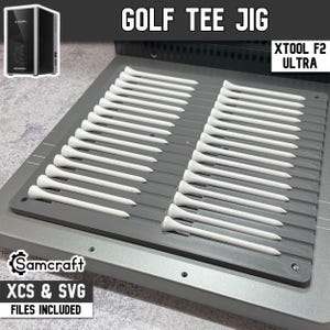 May include: A gray plastic golf tee jig designed for the xTool F2 Ultra, featuring two columns of slots holding twenty-four white golf tees. The jig is labeled with the text GOLF TEE JIG, XTOOL F2 ULTRA, and Samcraft XCS & SVG FILES INCLUDED.
