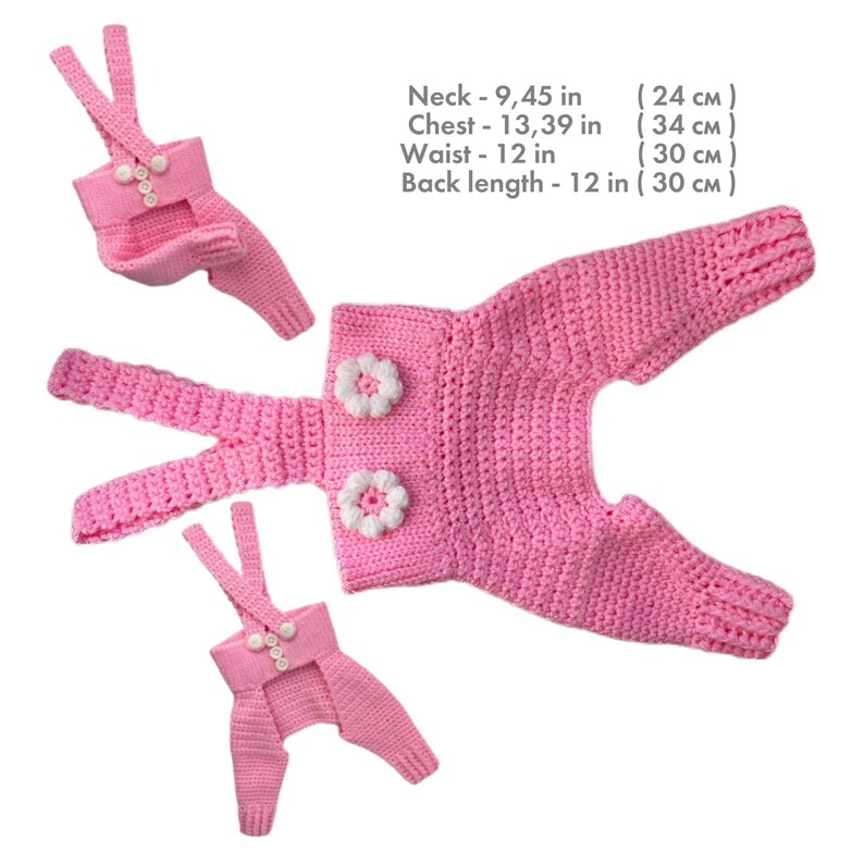 May include: Three pink crocheted overalls with white flower accents and straps. Text: Neck - 9.45 in, Chest - 13.39 in, Waist - 12 in, Back length - 12 in. The garments feature a textured knit pattern and button closures on the straps.