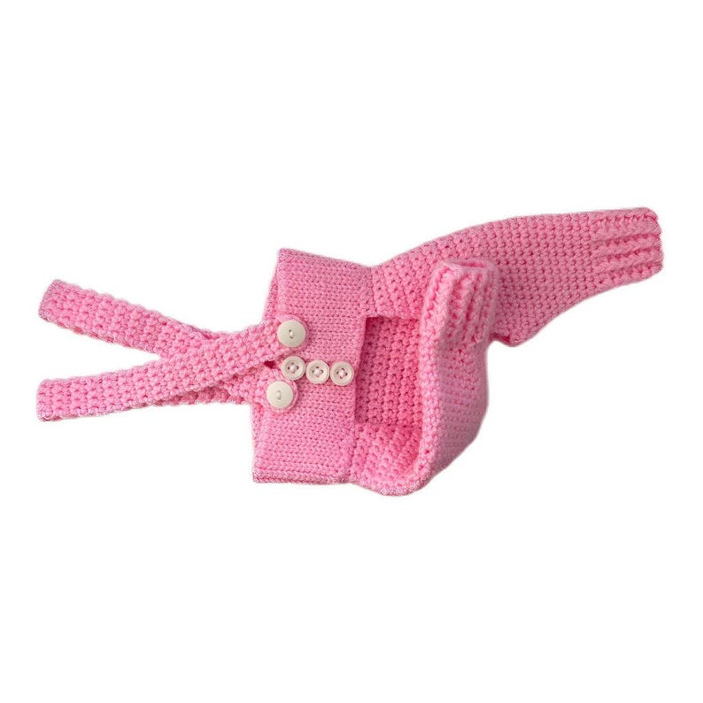 May include: A bright pink crocheted garment featuring long sleeves and a structured bodice. The front includes two adjustable straps that fasten with three small white buttons, creating a secure closure for this textured knit piece.