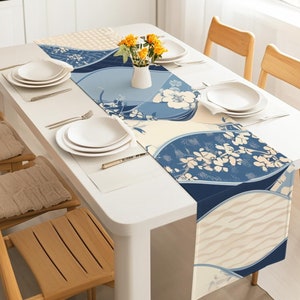 Puede incluir: Una mesa blanca con un camino de mesa estampado en azul y blanco con un diseño floral. El camino de mesa está sobre una mesa blanca con dos sillas a cada lado. Hay platos y cubiertos en la mesa.