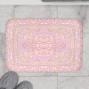 May include: A pink and gold bath mat with an intricate floral pattern. The mat has a border with a repeating design.