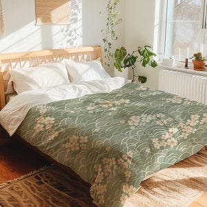 May include: A green and white duvet cover with a floral pattern. The duvet cover features a repeating pattern of white flowers and green waves. The duvet cover is on a bed with white pillows.
