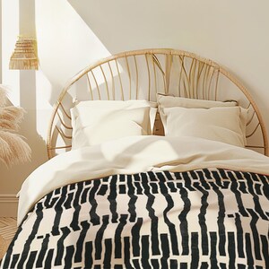 May include: A bed with a white headboard and a black and white patterned duvet cover. The headboard is made of woven rattan and has a curved shape.