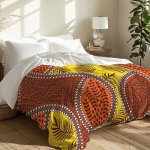 May include: A yellow, orange, and brown patterned duvet cover with a geometric design featuring leaves and circles. The duvet cover is on a bed with white bedding.