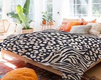Puede incluir: Un juego de cama negro y blanco con estampado de leopardo y cebra. La ropa de cama está en una cama con un marco de madera y está decorada con almohadas naranjas.