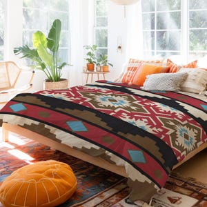 Pode incluir: Uma cama com uma capa de edredom com padrão geométrico vermelho, marrom, branco e azul. A cama está em um quarto com paredes brancas e janelas grandes.
